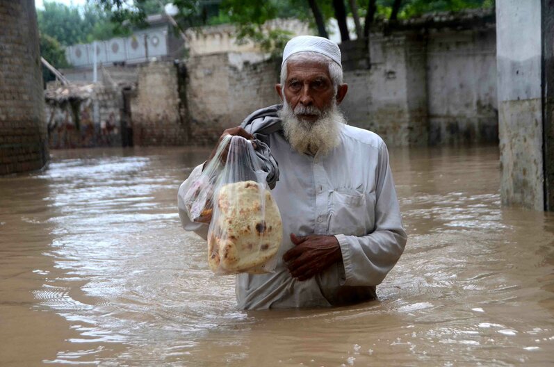 In this photo a man wades through a flooded area in Peshawar carrying bread, Khyber Pakhtunkhwa, Pakistan. Thousands of people who live in areas under threat of flooding have been told to evacuate. Credit: Hussain Ali / ANADOLU AGENCY / Anadolu Agency via AFP 
