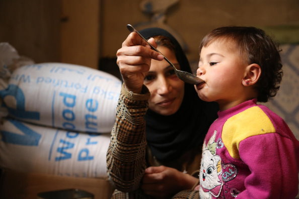 سيدة نازحة مع أسرتها من دوما في ريف دمشق إلى عدرا  تطعم ابنتها البالغة من العمر 18 شهرًا. الصورة: برنامج الأغذية العالمي / عبير عطيفة