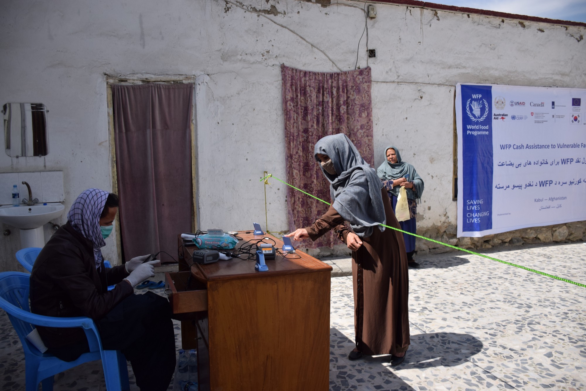 أفغانستان: سيدة تتلقى المساعدات النقدية وهي تحافظ على التباعد الاجتماعي لتجنب انتشار العدوى. صورة/نفيسة رشتين