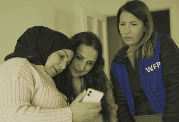 Two young women look at a mobile phone screen with a woman wearing a blue WFP vest