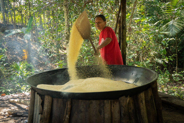 Indigenous woman in red T-shirt roasts yucca flour on an open fire in the Colombian Amazon