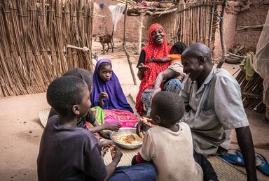 a family is sitting on the ground and eating their meal