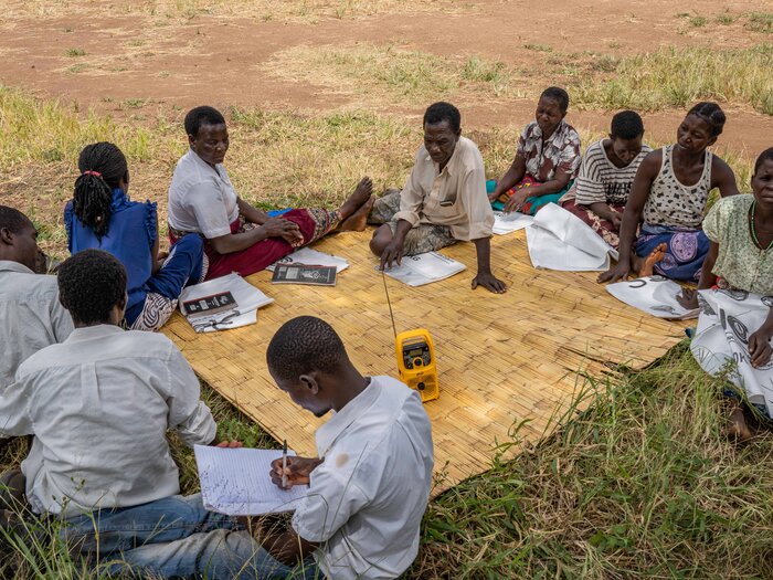 A group of people sitting around a radio on the ground