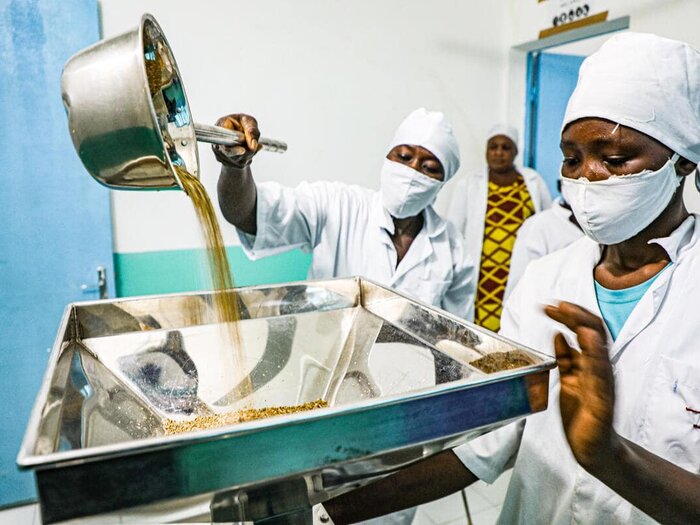 Members of the fortified infant flour processing unit in Ouallam (Tillabéry region) pour the roasted millet grains into the grinding mill for the production of fortified flour.