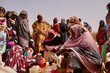 At a desert-like distribution site, women in colourful gowns collect WFP food assistance including vegetable oil. Photo: WFP