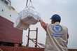 The back of a man wearing a WFP vest and cap managing cargo being unloaded from a ship. Photo: WFP/Alaa Noman