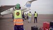 A WFP-managed UNHAS plane sits on an airport tarmac, as passengers disembark and airport workers unload bags. Photo: WFP