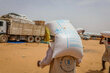Workers carry bags of WFP food in a sandy landscape, with trucks and other vehicles in the background. Photo: WFP/Arete/Salamon Djek