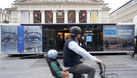 A biker, with a small child in the back, whizzes past a large poster of a Gaza exhibit on a public space. Photo: WFP