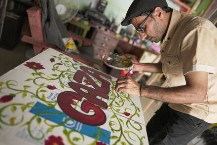 Person paints decorative artwork with WFP logo on a large board, using a brush and palette in a workshop setting, highlighting creative engagement and advocacy.