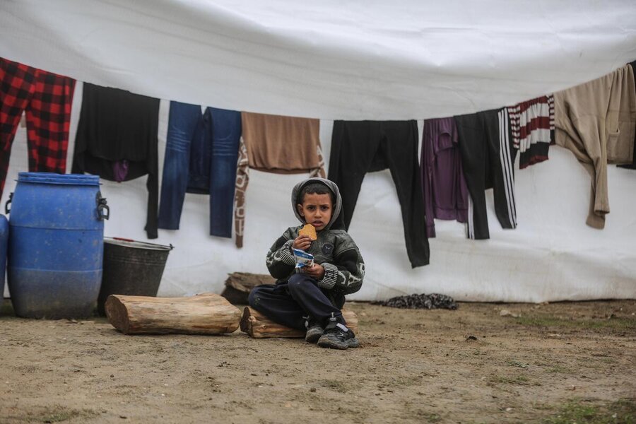 A child eats bread sitting on the ground outside a tent in Gaza