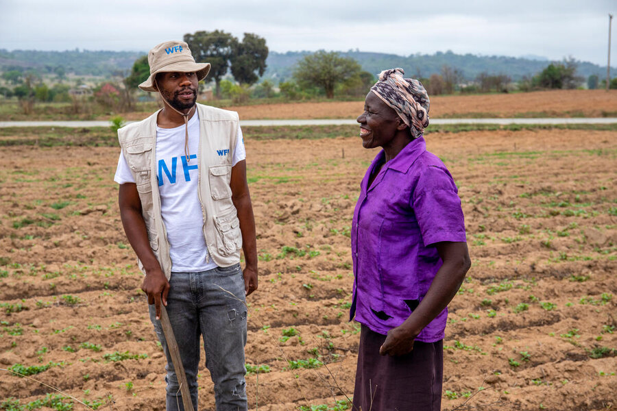 A WFP staff member stands next to a woman farmer in a purple shirt in a brown field in Zimbabwe