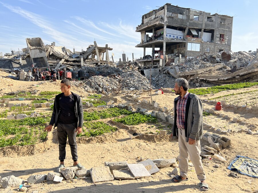 Nabil Azab (R) stands near the greens his family is tending. Behind are the remains of the apartment building his family still lives in - despite the danger. WFP/Jonathan Dumont