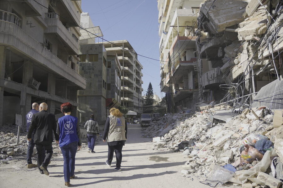 A group in humanitarian vests walk up a street past bombed building