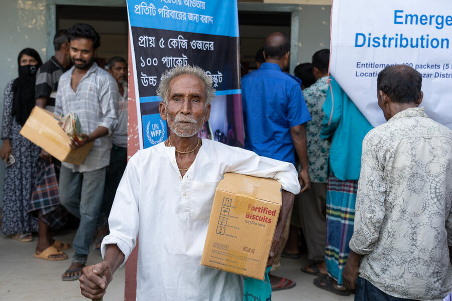 A man with a white goatie beard in Bangladesh walks away with a box form a food distribution point