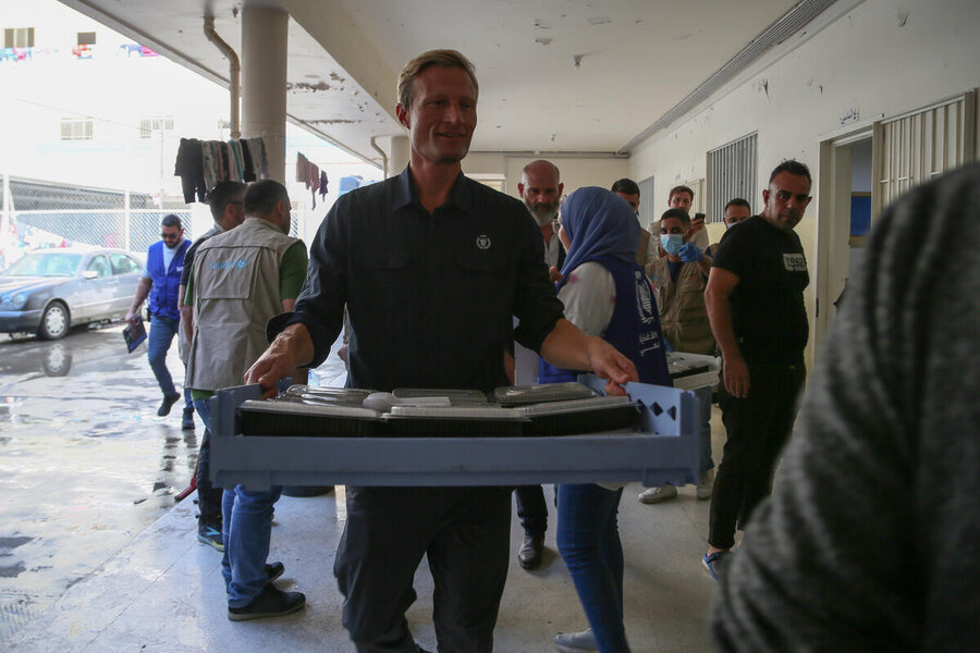 A man in a WFP shirt carries a big tray of school meals packs