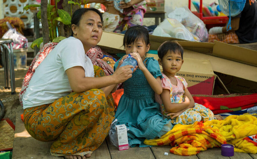 Woman kneels as girl drinks from bottle and little boy looks on