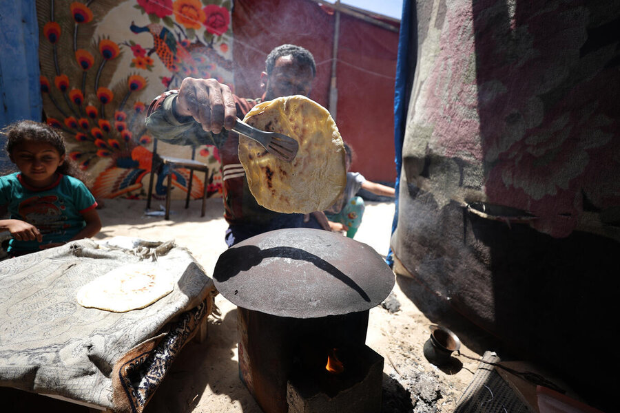 A man holds a flatbread in front of a makeshift stove in a refugee camp