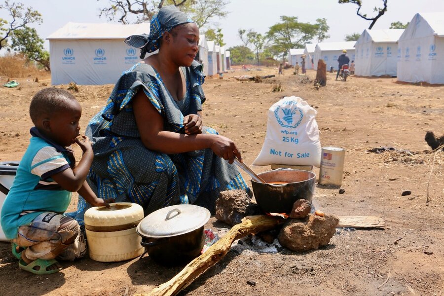 In Cameroon, Central African refugee Fatouma stirs a pot where she's cooking up a WFP-supported meal, as her young son looks on. Photo: WFP/Mayramou Madaki