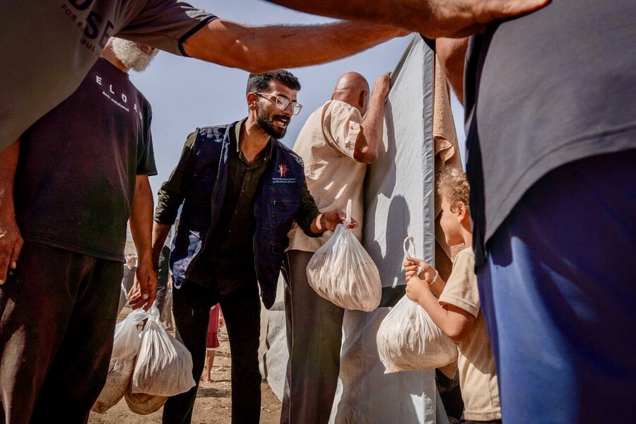 A small child smiles as a man delivers a package of pita bread. Photo: WFP/Maxime Le Lijour 