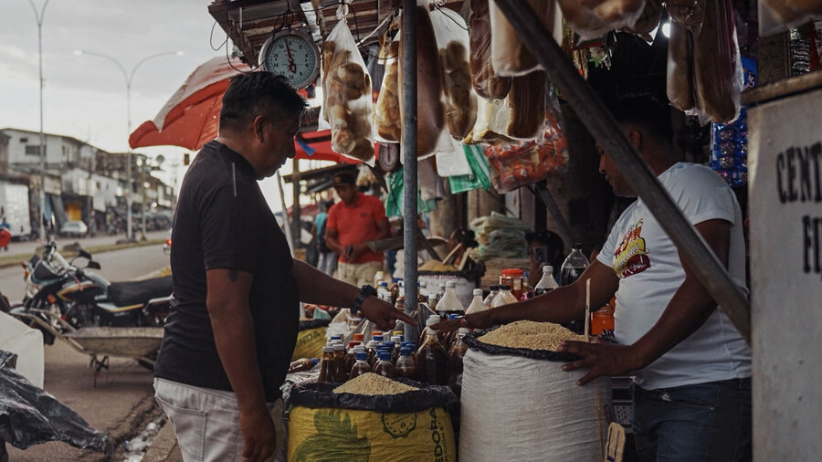 Indigenous man in a dark blue shirt buys something at a market stall in Venezuela