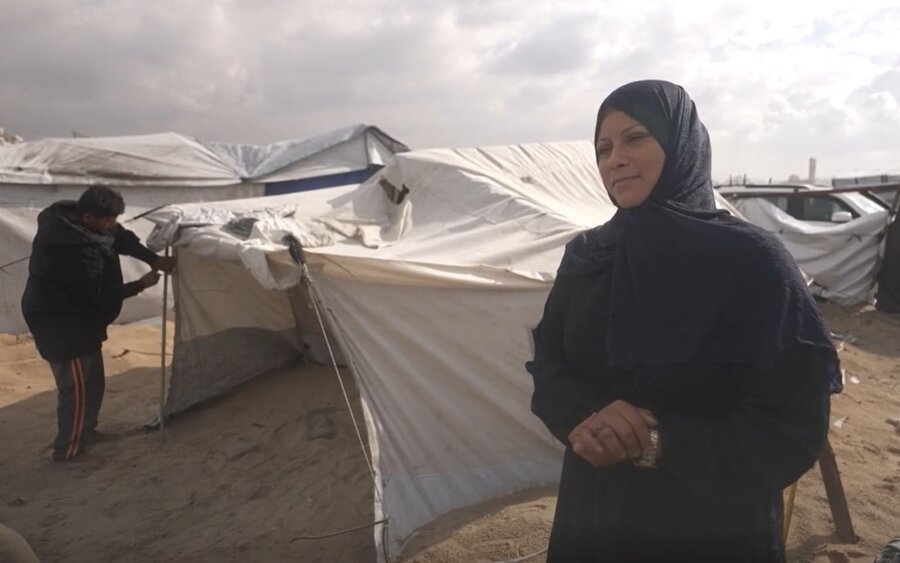 A Palestinian woman standing in front of a tent in a field of tents