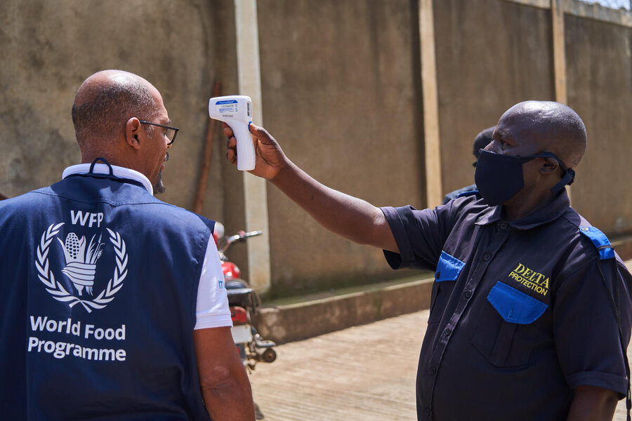 A man wearing a blue WFP vest is scanned for fever by a security guard wearing a blue uniform and mask. Photo: WFP/Gedeon Mugisa