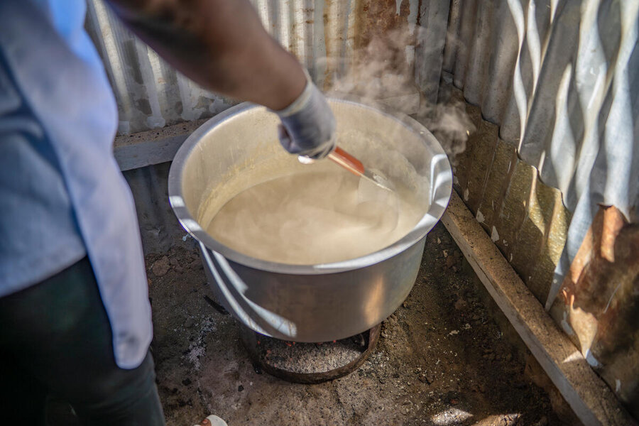 A closeup of a pot of porridge being stirred by a person with a blue uniform and gloves. Photo: WFP/Michael Castofas
