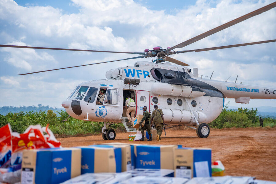 A white WFP helicopter on a dirt tarmac in the background, with boxes of aid in the foreground. Photo: WFP/Michael Castofas
