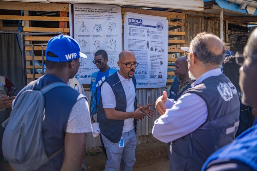 Men in blue vests speak to each other standing outside a health centre in northeastern DRC. Photo: WFP/Michael Castofas