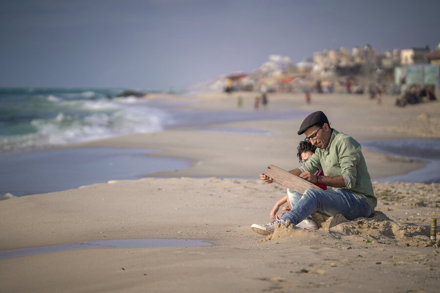 A man and a boy sit on a beach, as waves come in. The main is painting. Photo: WFP/Jaber Badwan