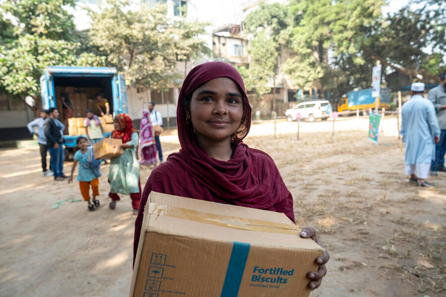 Copilot said:  Person holds a box of fortified biscuits during an aid distribution, while people collect relief supplies from a truck in the background.