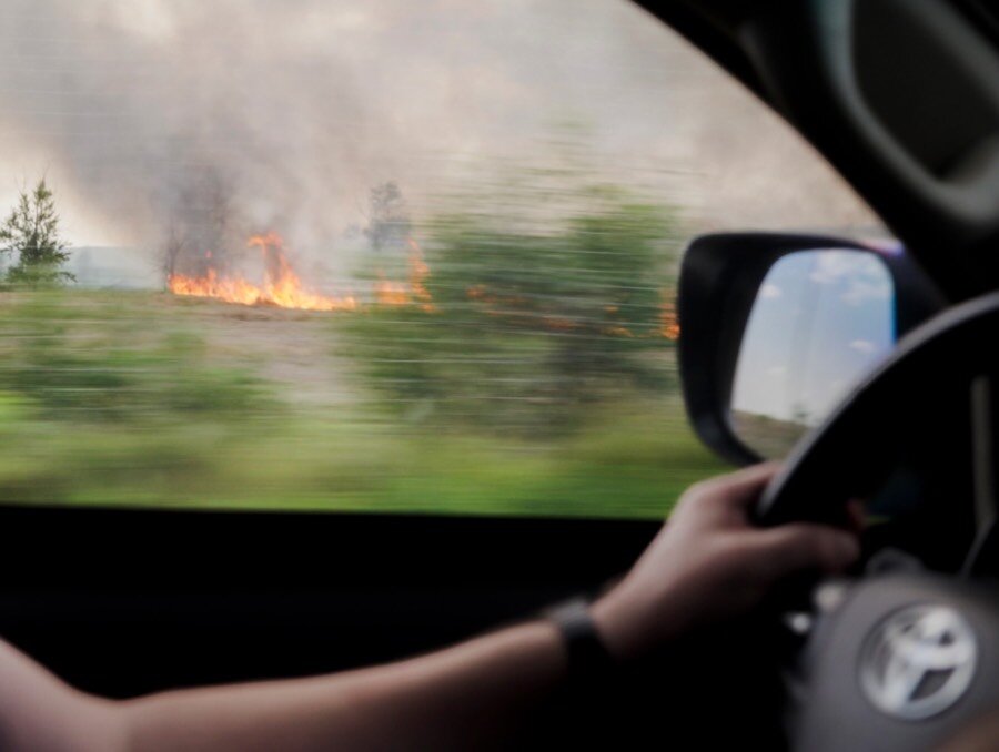 A closeup of a hand on the steering wheel, with image of a spreading fire through the vehicle's side window. Photo: WFP/Sayed Asif Mahmud