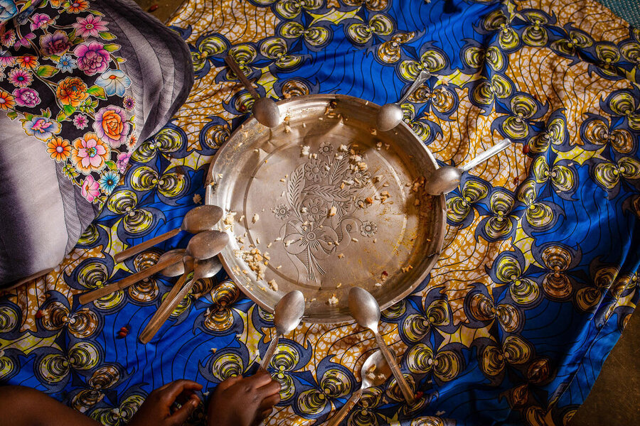 An empty metal serving tray surrounded by spoons rests on a patterned cloth after a shared meal has been eaten.